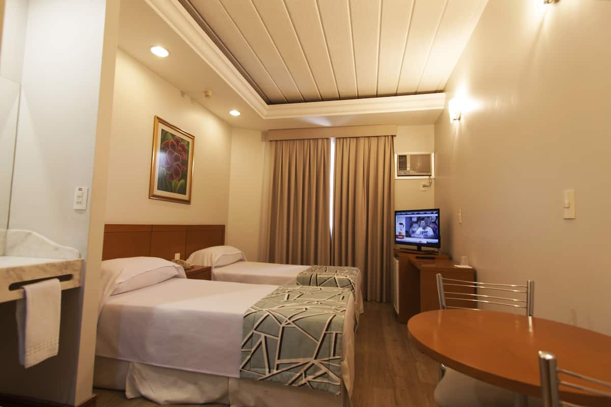 Une chambre d’hôtel avec deux lits, une table en bois, un téléviseur et un tableau au mur.