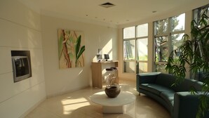 A modern living room with a curved sofa, a coffee table, a desk with computers, and a large window. - Di Giulio Hotel (São José dos Campos)