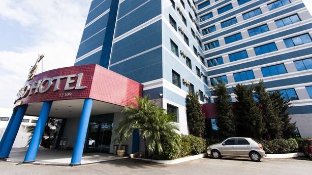 A hotel with a modern design, featuring a prominent red and blue facade, large windows, and a parking area with a car. - Di Giulio Hotel (São José dos Campos)