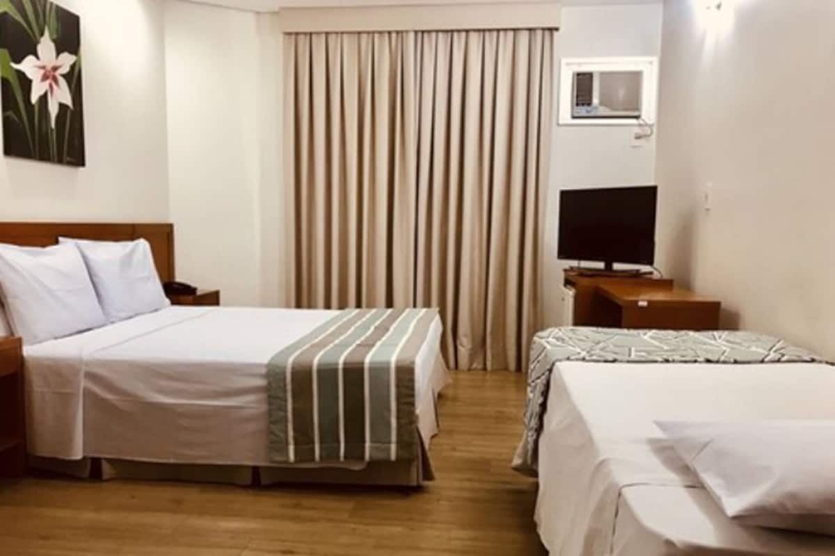 Une chambre d’hôtel avec deux lits, une télévision et une fenêtre avec des rideaux.