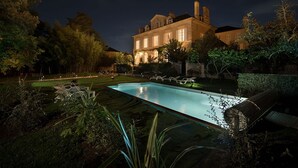A large, illuminated mansion with a swimming pool, surrounded by lush greenery and trees. - La Maison de Maître (Fontenay-le-Comte)