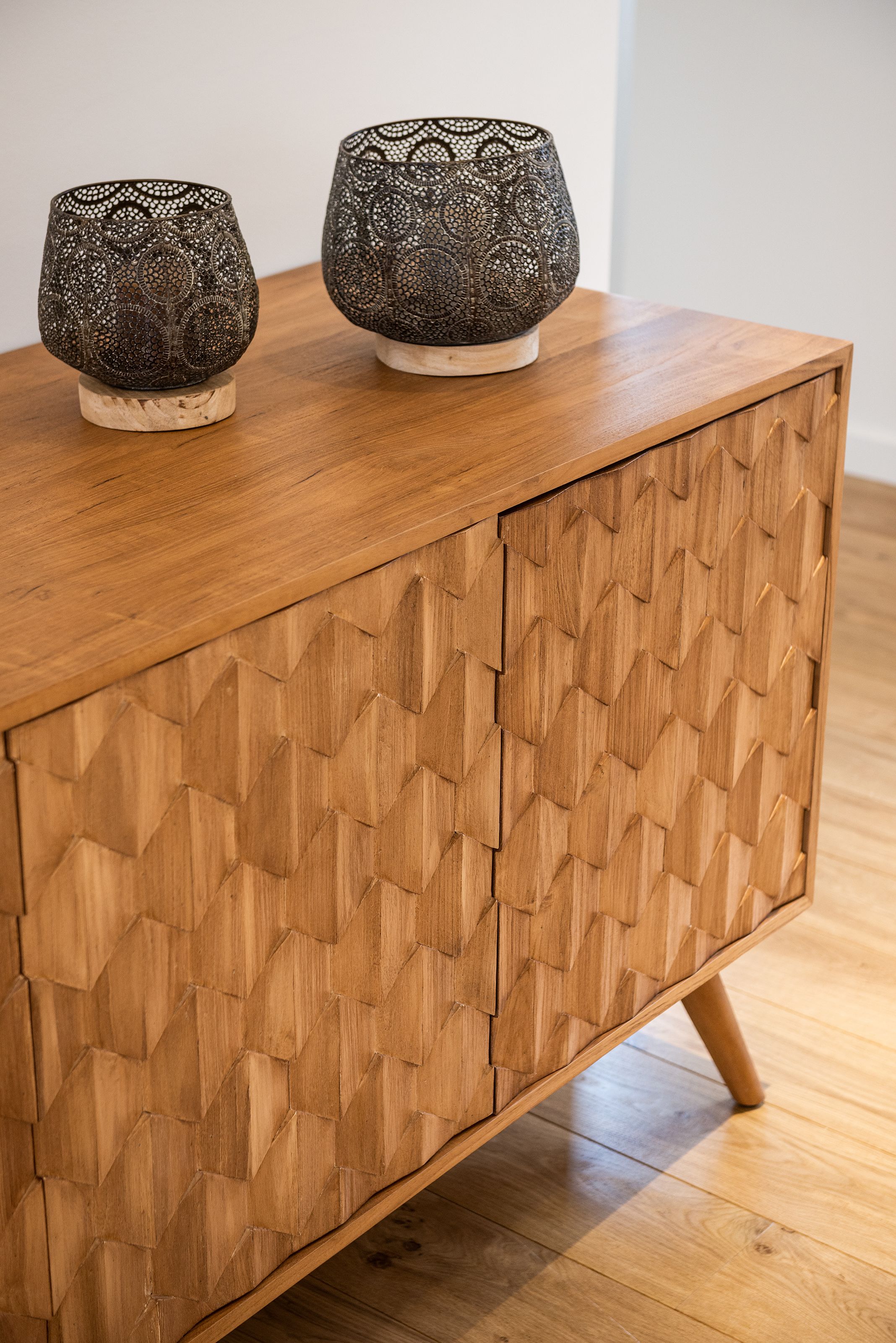 Un meuble en bois orné d’un motif géométrique et surmonté de deux bols décoratifs.