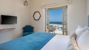 A hotel room with a bed, a television, a view of the beach, and a chair by the window. - Avra Apartments Kolymbari Harbour (Platanias)