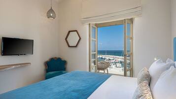 Habitación de hotel con cama, televisión, vista a la playa y una silla junto a la ventana.