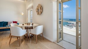A modern living room with a dining area, a sofa, and a view of the sea through a large glass door. - Avra Apartments Kolymbari Harbour (Platanias)