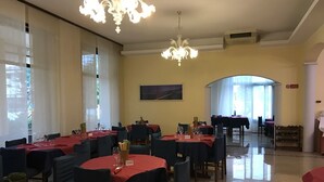 Uma sala de jantar com mesas redondas cobertas por toalhas vermelhas, cadeiras e lustres.