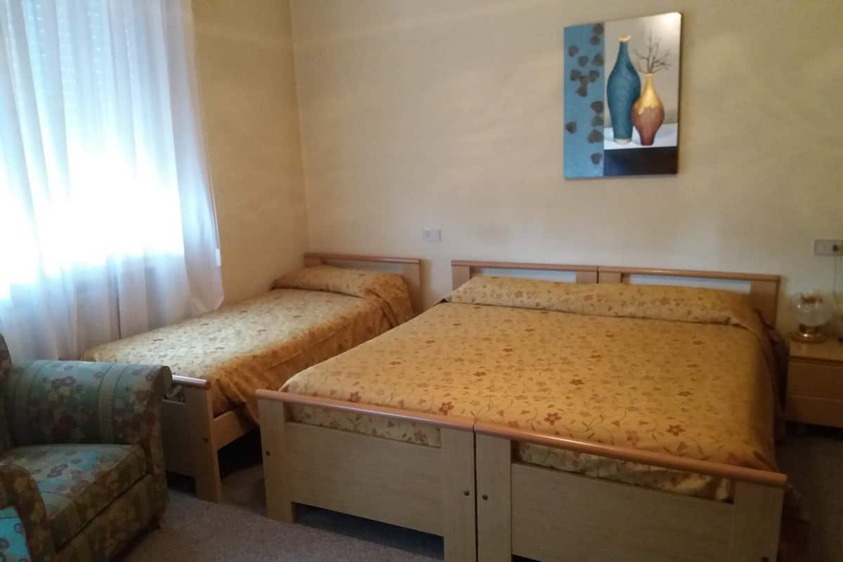 Een slaapkamer met twee eenpersoonsbedden, een stoel, een nachtkastje en een schilderij aan de muur.