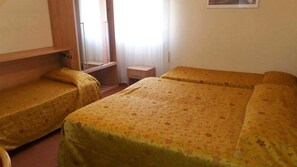 Una habitación con dos camas individuales, un escritorio de madera pequeño y una ventana con cortinas.