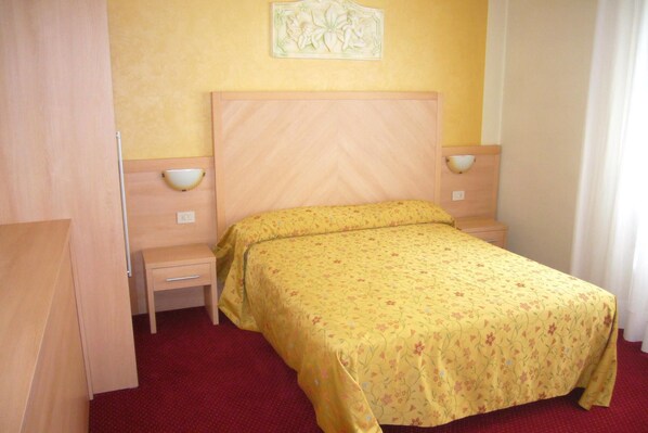 A hotel room with a bed, a nightstand, a wall-mounted light, and a door.