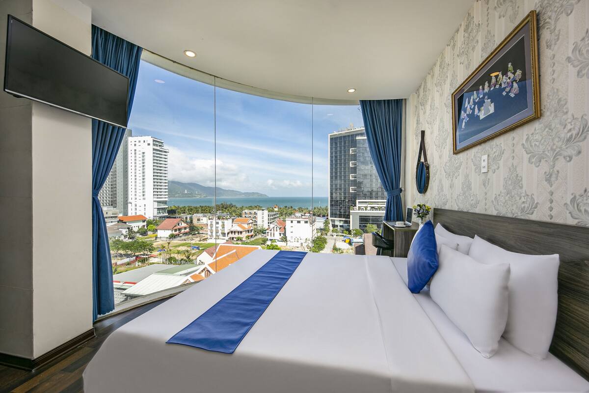 A hotel room with a large bed, a view of the city, and a painting on the wall.
