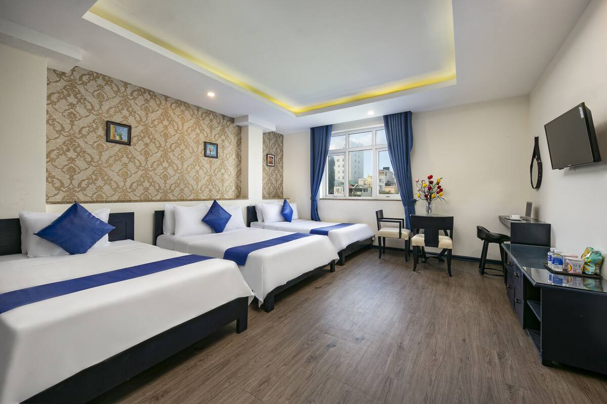 A hotel room with three beds, a desk, a chair, and a TV.