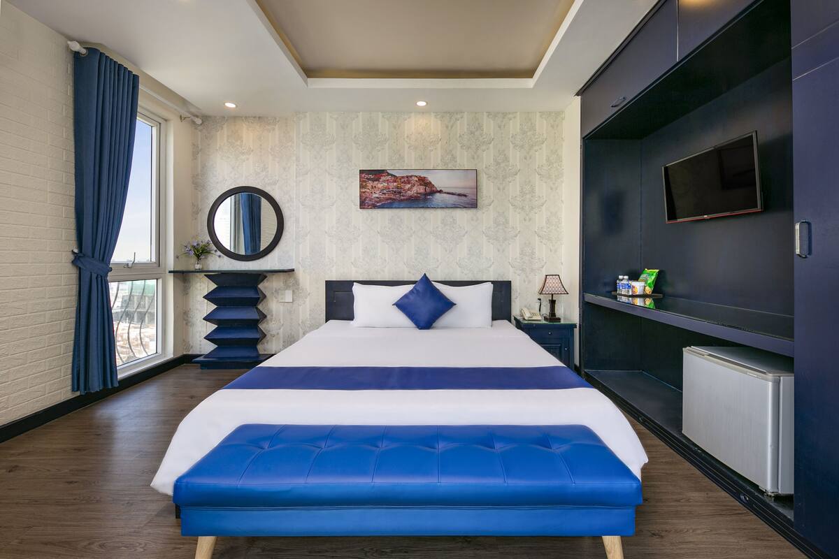 A modern hotel room with a large bed, a TV, a small desk, and a view of the outdoors.