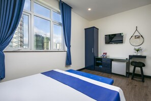 A hotel room with a bed, a desk, a TV, and a view of the cityscape. - Alibaba Hotel (Da Nang)