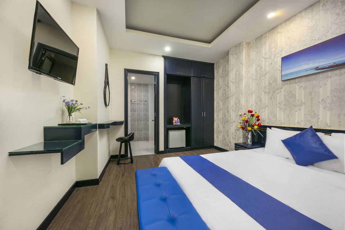 A hotel room with a bed, a TV mounted on the wall, a desk with a chair, and a wardrobe.