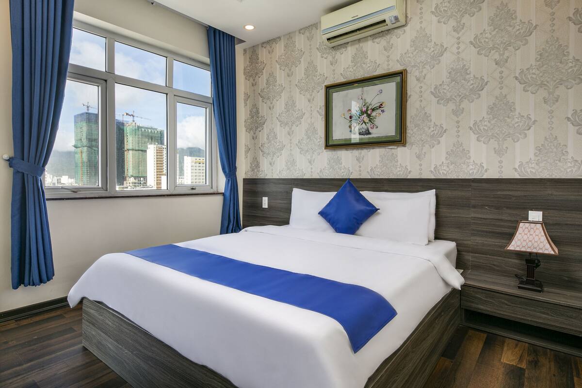 A hotel room with a large bed, a nightstand, a lamp, a framed picture, and a window with curtains.