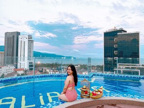 A woman sitting by a pool with a cityscape in the background. - Alibaba Hotel (Da Nang)