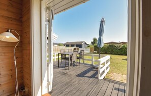An open door to a wooden deck with a table and chairs, a white fence, and a view of a house in the background. - 2 bedroom beautiful home in Nyborg (Nyborg)