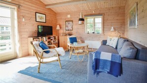 Interior acolhedor de uma cabana com sofá, cadeiras, televisão e estante de livros.