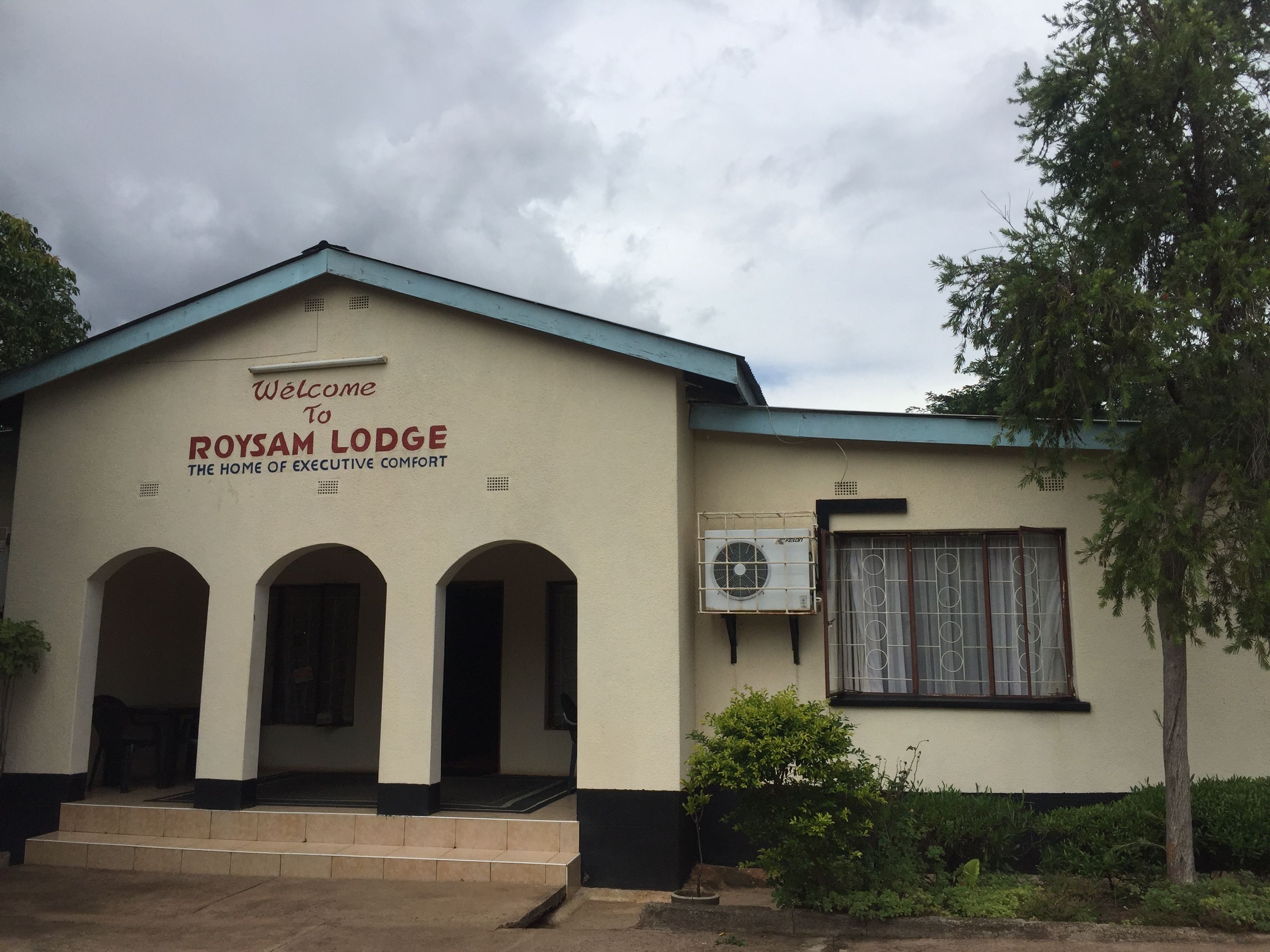 A building with a sign reading "Welcome to ROYSAM LODGE - The Home of Executive Comfort."