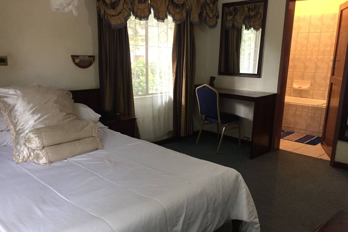 A hotel room with a large bed, a desk, a chair, and a bathroom visible through an open door.