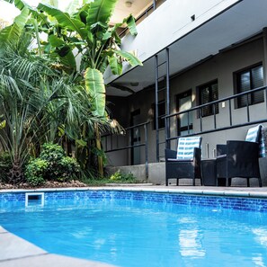A swimming pool with lounge chairs and a building with balconies. - Hillside Executive Accommodation (Windhoek)