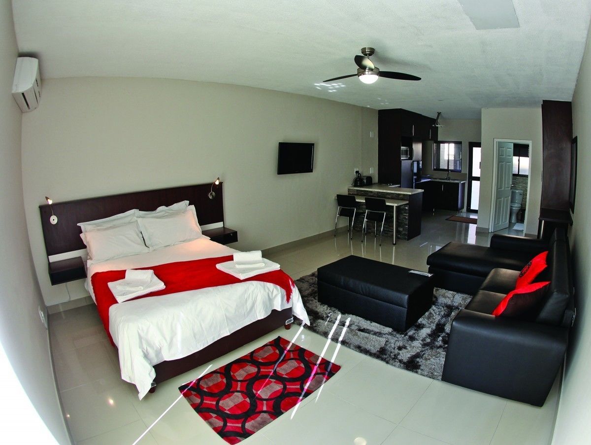 A modern hotel room with a large bed, a sofa, a dining area, and a kitchen.
