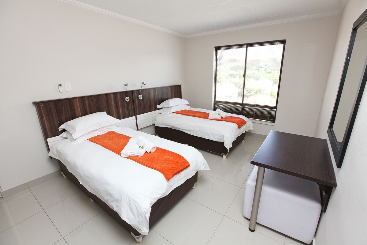 A hotel room with two beds, a desk, and a large window.