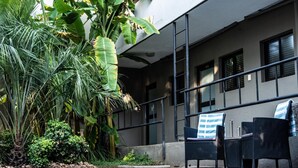 A swimming pool with lounge chairs, surrounded by tropical plants and a modern building. - Hillside Executive Accommodation (Windhoek)