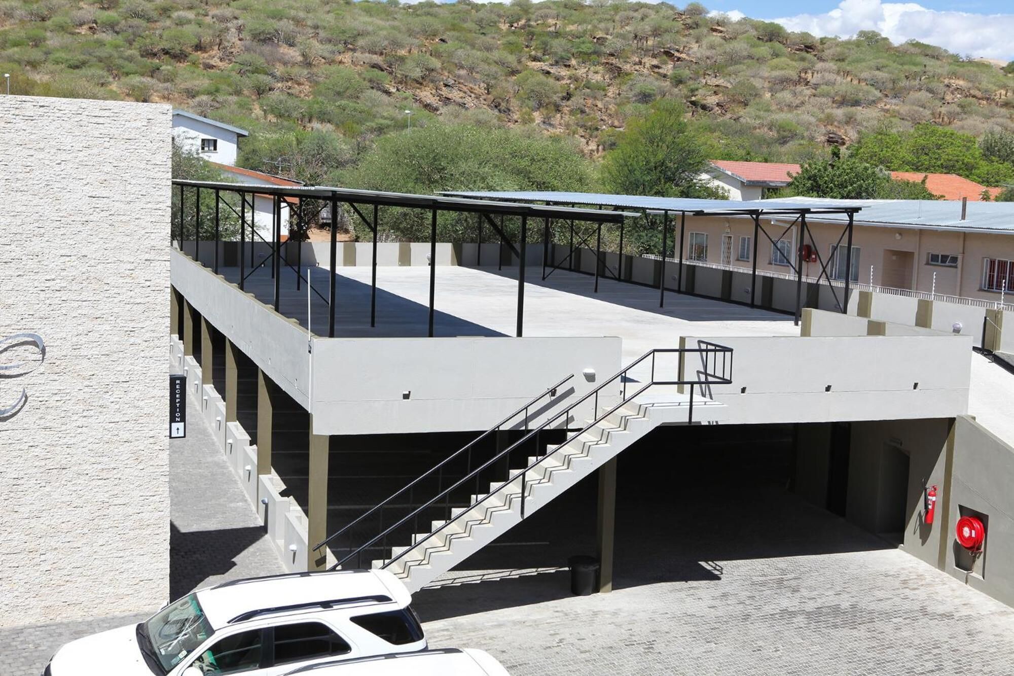 Un edificio moderno con techo plano, un espacio exterior cubierto con escaleras, y un coche estacionado al frente.