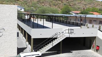 Un edificio moderno con techo plano, un espacio exterior cubierto con escaleras, y un coche estacionado al frente.