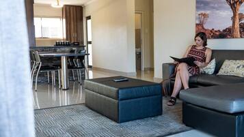 A modern living room with a sofa, a coffee table, and a dining area with chairs and a kitchen in the background.