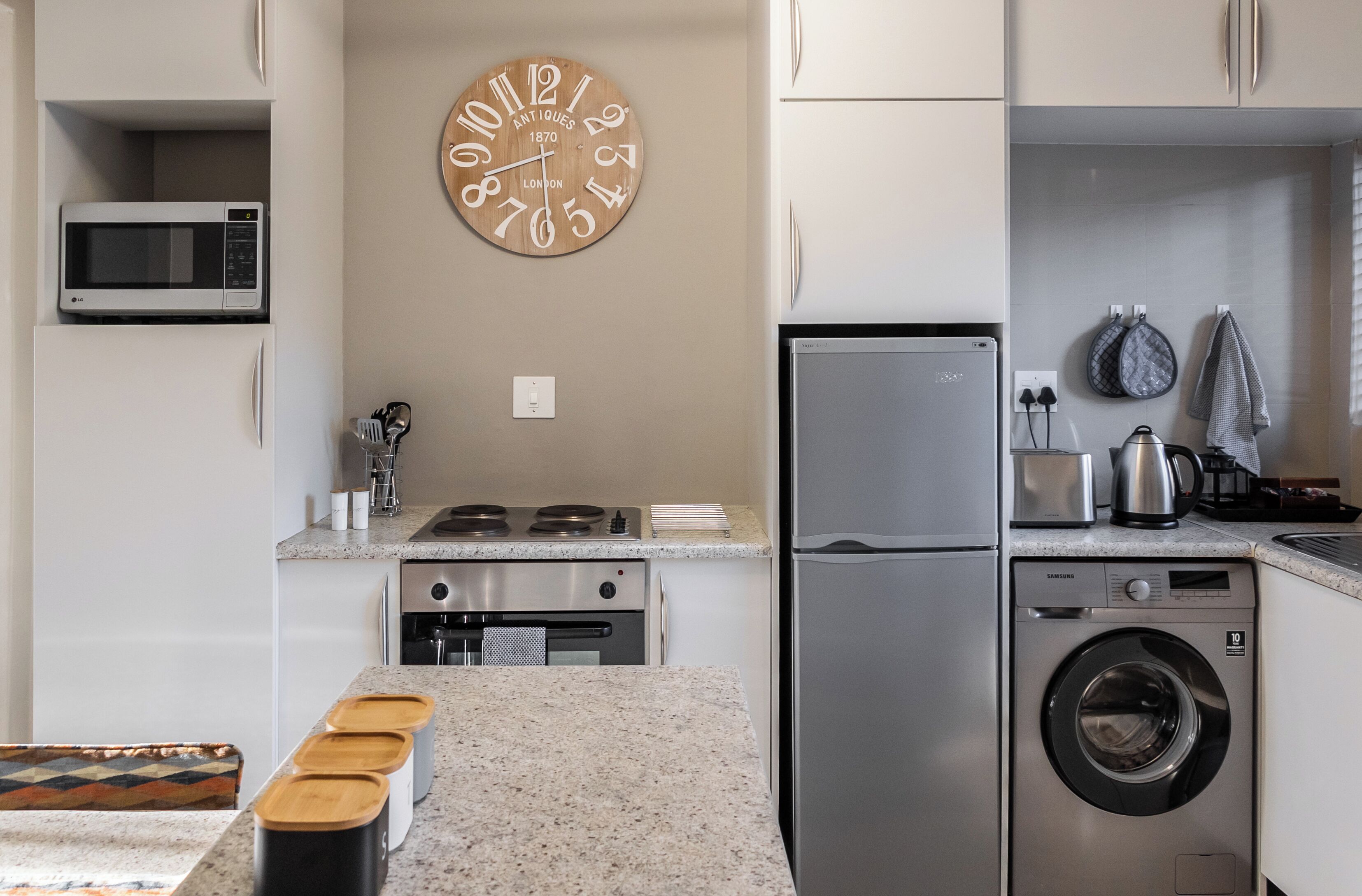 Una cocina moderna equipada con microondas, estufa, horno, lavadora y un reloj de pared.