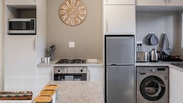 Una cocina moderna equipada con microondas, estufa, horno, lavadora y un reloj de pared.
