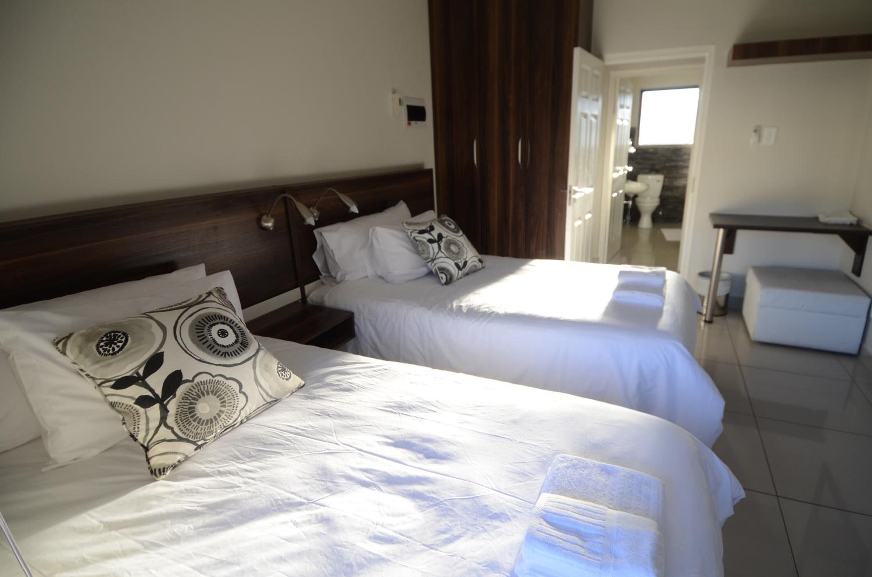 Habitación de hotel con dos camas, cabecero de madera, una mesita y vista al baño.