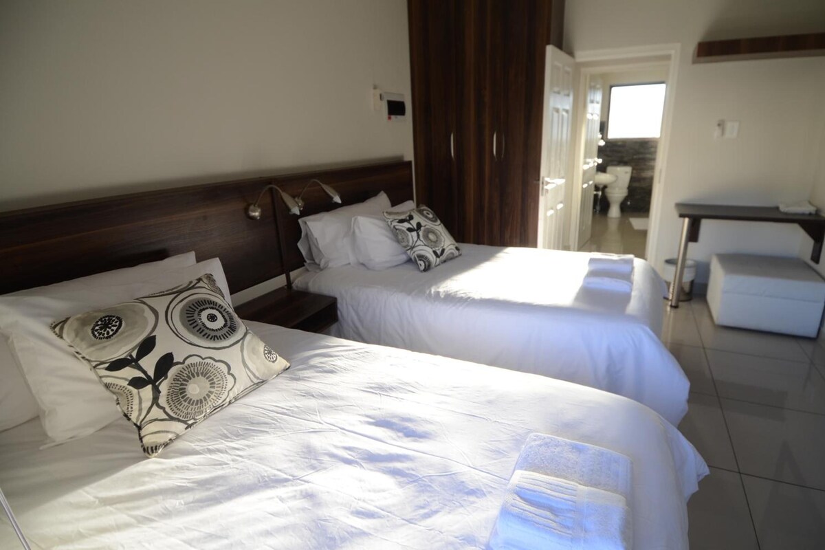 A hotel room with two beds, a wooden headboard, a small table, and a view of the bathroom.