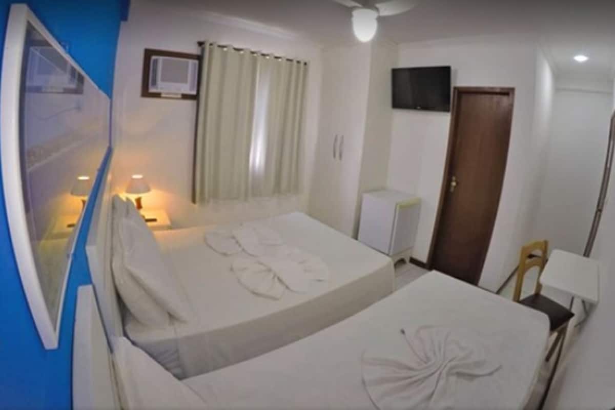 Une chambre d’hôtel avec un lit, un bureau, une chaise, une télévision et une fenêtre avec des rideaux.