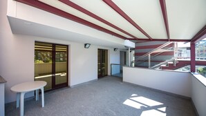A spacious balcony with a glass door leading to an outdoor area, a small table, and a staircase. - Piazzi House (Sondrio)
