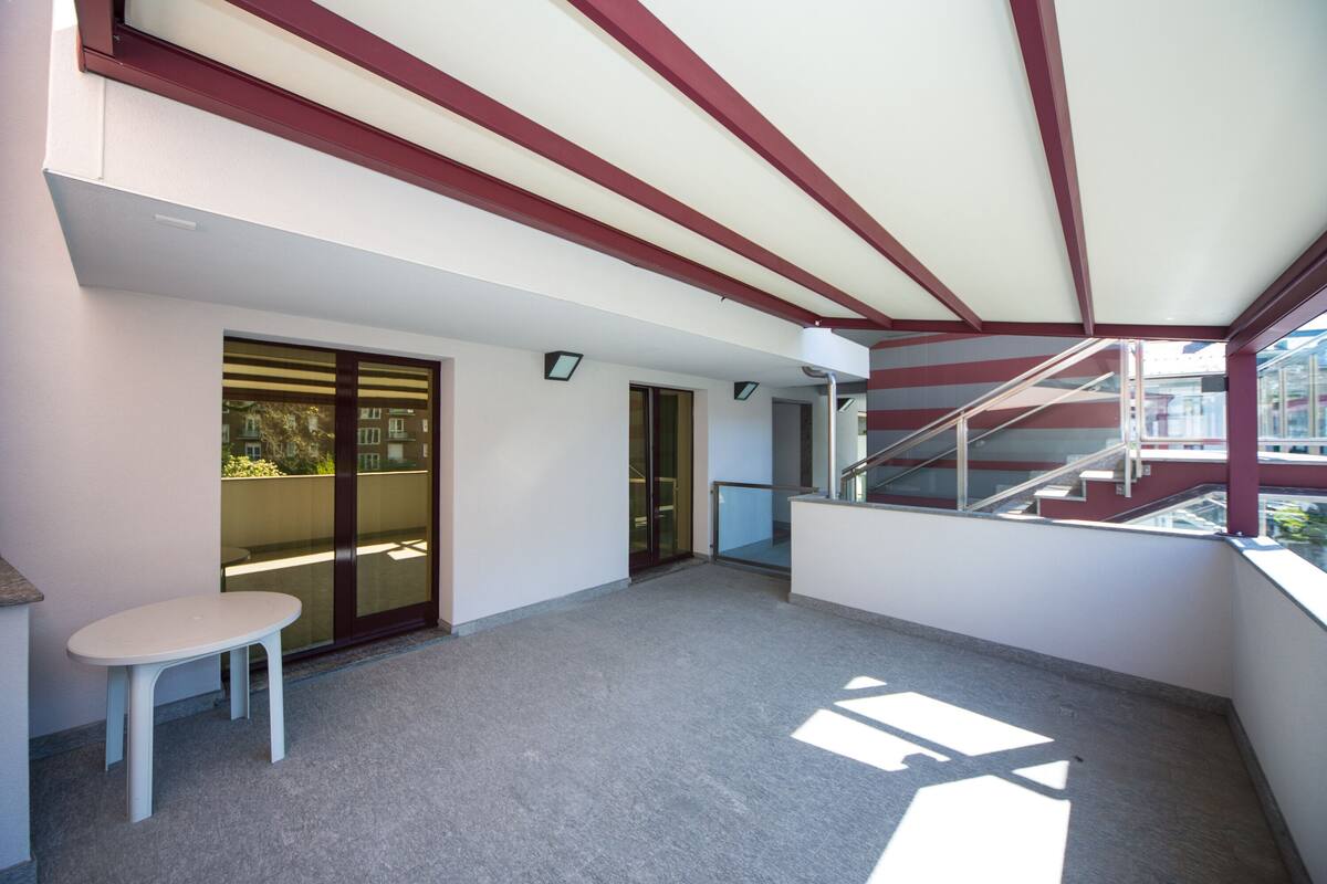 A spacious balcony with a glass door leading to an outdoor area, a small table, and a staircase.