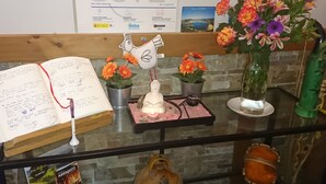 Un escritorio con un cuaderno, una estatua de Buda, una pequeña estatua de Buda, un florero con flores, un cuenco decorativo y un libro.