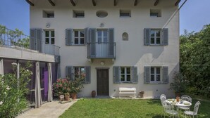 Ein zweistöckiges Gebäude mit Balkon, kleinem Garten und einer Terrasse mit Gartenmöbeln.