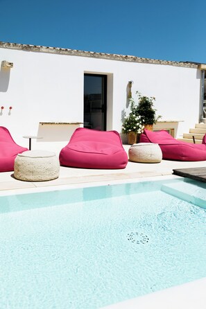 Un área de piscina con sillones tipo bean bag color rosa y una pared blanca al fondo.