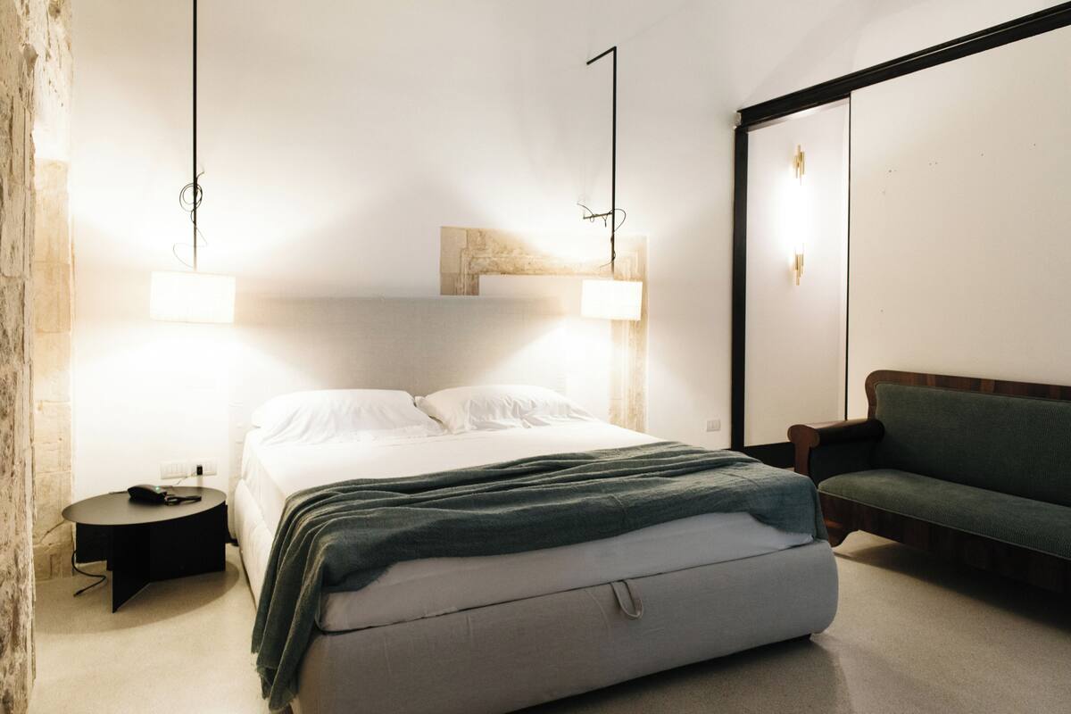 A modern bedroom with a bed, bedside table, and a green sofa.