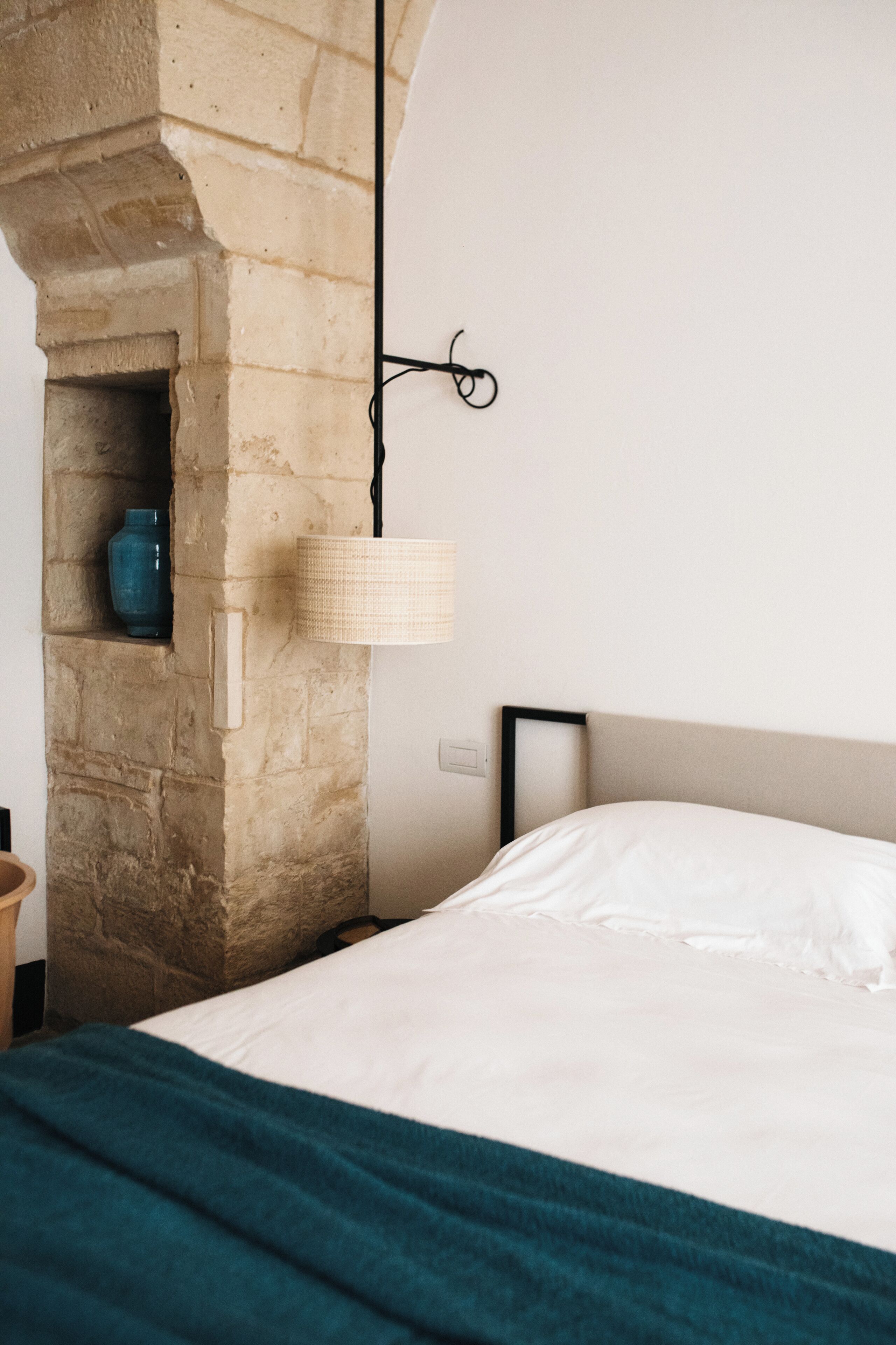 Quarto com lareira de pedra, luminária pendente e cama com manta azul-turquesa.