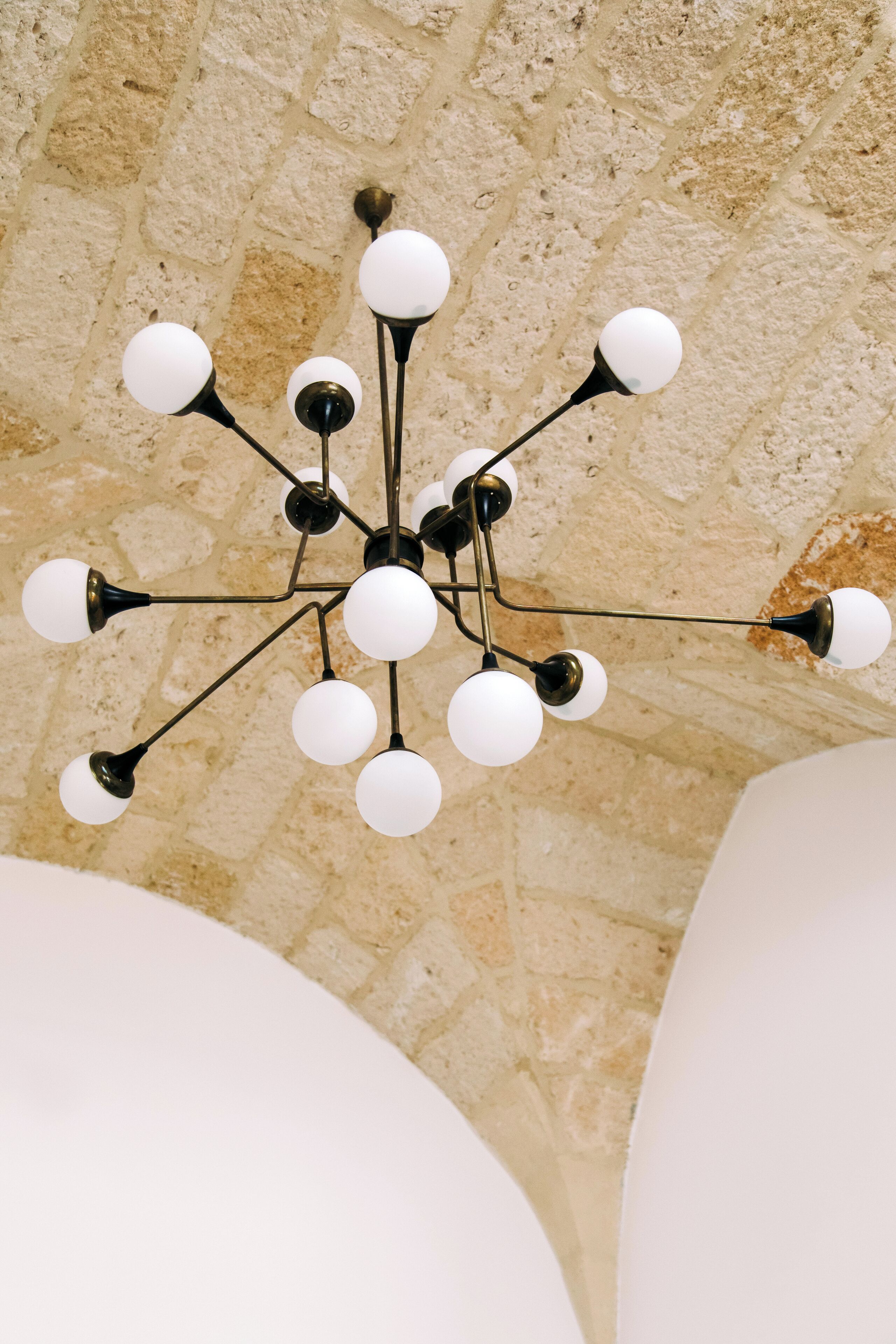 A chandelier with multiple spherical lights against a stone wall.