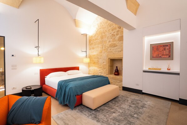 A modern hotel room with a stone accent wall, a large bed with a red headboard, a bench, a small table, and a framed picture on the wall. - Palazzo De Noha (Lecce)