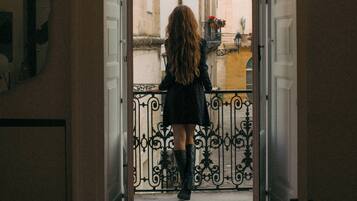 A hallway leading to a balcony with wrought iron railings and a view of buildings.