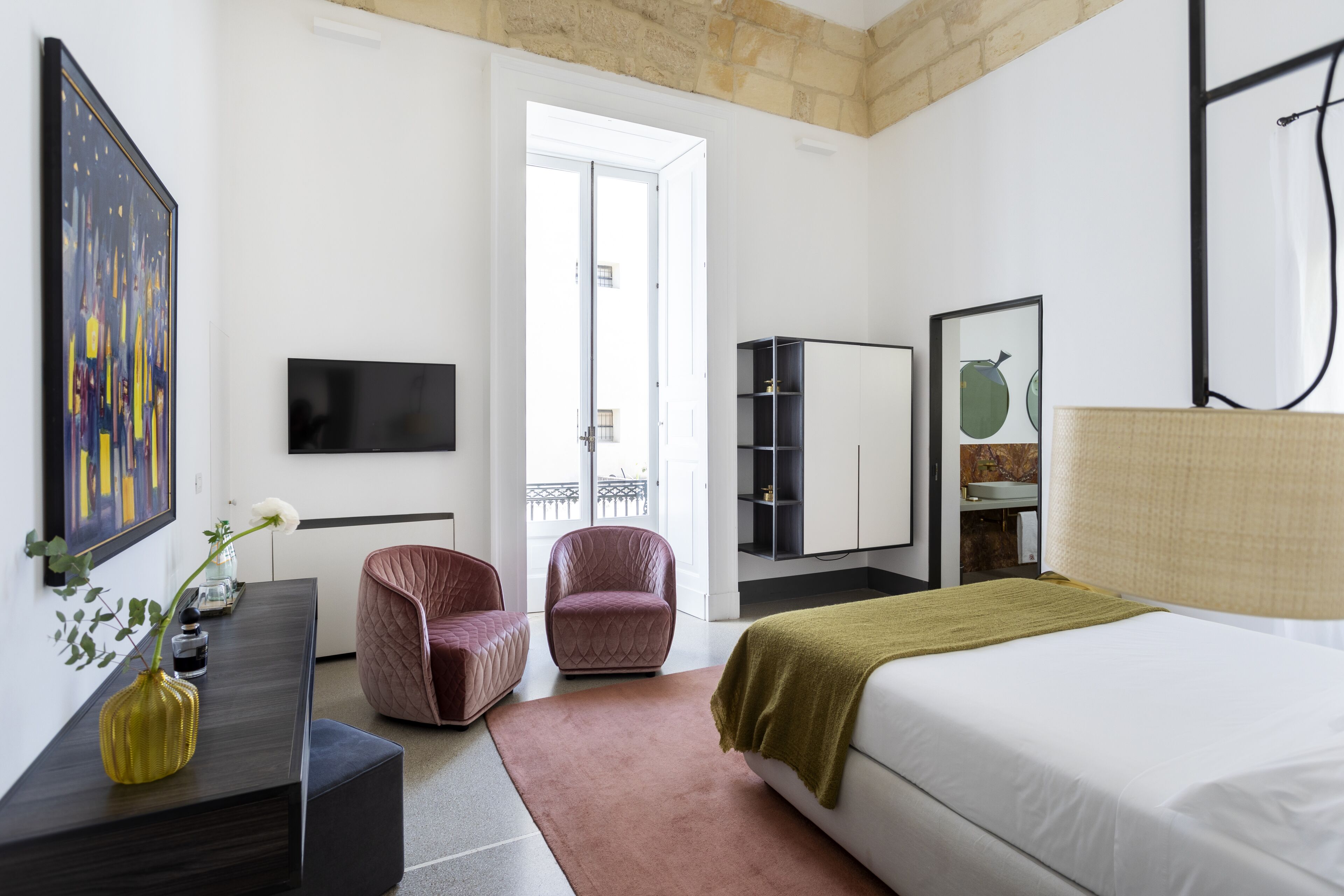 Une chambre d’hôtel moderne équipée d’un lit, d’un bureau, d’une chaise, d’une télévision, d’une armoire et offrant une vue sur le balcon.