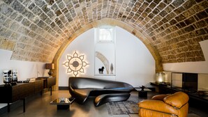 A modern living room with a stone vaulted ceiling, a black leather sofa, an orange leather armchair, and a decorative wall piece. - Palazzo De Noha (Lecce)