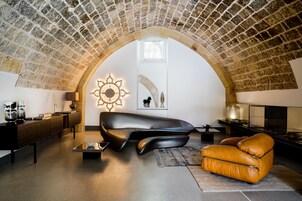 Uma sala de estar moderna com teto abobadado de pedra, um sofá de couro preto, uma poltrona de couro laranja e uma peça decorativa na parede.