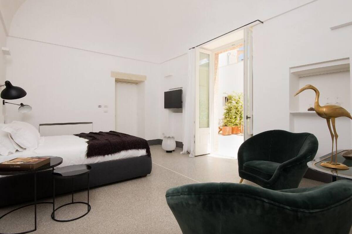 A modern bedroom with a bed, a desk, a chair, a TV, and a door leading to a balcony.